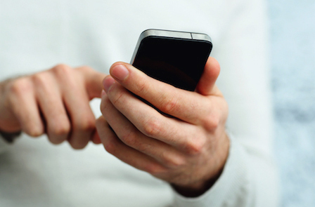 Closeup image of a male hand holding smartphone and typing on it